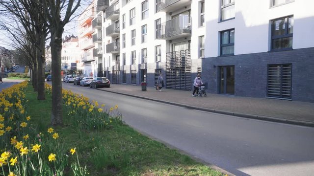 Old brave lady with face mask and walk reck moves slowly on the street in spring.