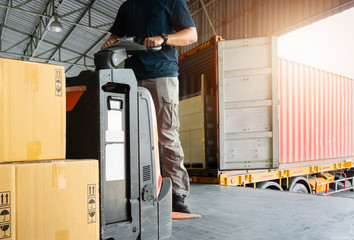 Worker courier is driving electric forklift pallet jack loading shipment goods, package boxes,...