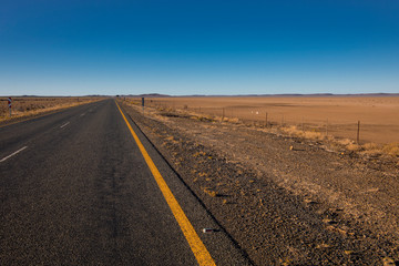 Fototapeta na wymiar An endless tarmac road, streching through the drought stricken Karoo, disappearing in the horizon. The freedom to travel. We will be free again. Tarmac road through the Karoo, South Africa