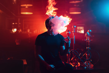 man smokes a hookah and lets out a cloud of smoke