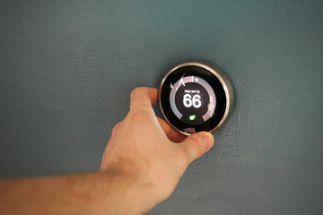 Hand adjusting temperature on electric thermostat. Temp set at 66 degrees to save money. Eco mode enabled!