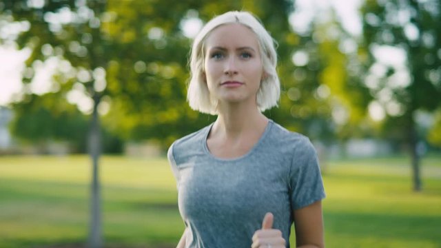 Confident and carefree young blonde woman runs in the park in slow motion