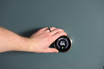Green tech- Electric thermostat to save money and energy. Hand present to make adjustments. - obrazy, fototapety, plakaty