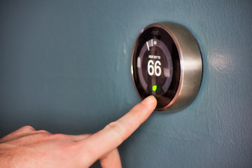 Hand operating smart thermostat to save money. Hand pushing eco mode to activate.