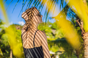 Young woman with the shadow of the palm leaf on her back. Relaxing on the seaside