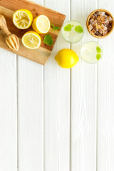 Homemade lemonade in glasses near juicer and cut lemons on white wooden background top-down copy space