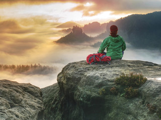 Alone girl sits with her back on cliff against huge misty mountain