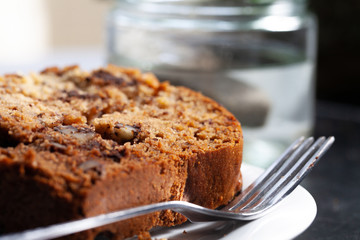 Slice of home made banana walnut cake on plate close-up with fork in front of a glass of green tea.