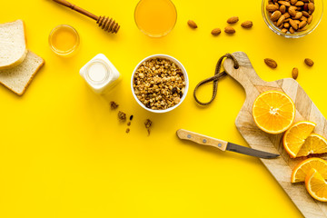 Morning granola near toast and oranges on yellow background top-down frame copy space