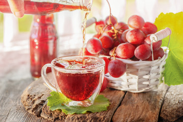 Grape juice from red grapes is poured from a bottle into a clear glass glass with a double bottom.