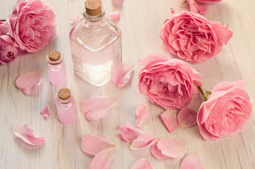 Rose water or oil in glass bottles with pink fresh rose flowers and petals on wooden background,...