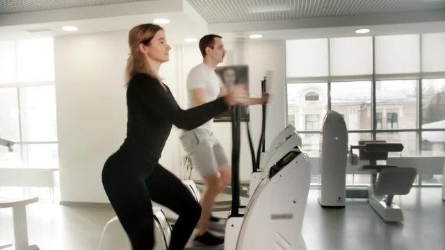 Sportive young man and woman in sportive clothes training their legs on exercise bike in modern gym