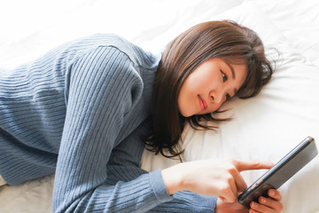 ベッドで寝る前にスマホを使う若い女性