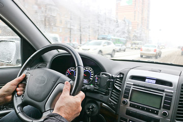 Fototapeta na wymiar Men's hands on the steering wheel of a car. The driver controls the car. View through the windshield. Car trips in winter.
