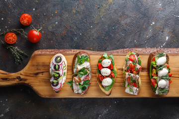 Bruschetta with tomatoes, bacon, herbs, mozzarella cheese , bell peppers, radishes and olives on an aged wooden Board. This is a classic Italian snack. Hot and crunchy bread