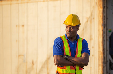 Cheerful factory worker man in hard hat smiling with arms crossed as sign of success blurred container box background