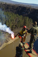 Man in a red helmet with a smoke bomb jumping with a rope. Ropejumping.
