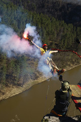 Man holding a smoke bomb in his hand jumps with a rope from a great height. Ropejumping.