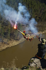 Man holding a smoke bomb in his hand jumps with a rope from a great height. Ropejumping.