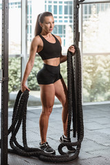 Portrait of fitness woman with battle rope in modern gym