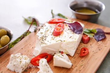 Tasty feta cheese with chili, herbs, spices and oil on board