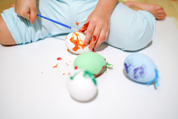 Having fun before Easter. Small children painting Easter eggs. Toddler playing with brush and paint on colorful eggs.