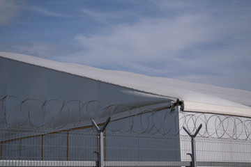 Hangar behind barbed wire. Canvas roof. Metal fence. Concept of a military base, insulator, refugee camp, prison.