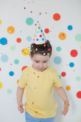 Toddler boy in the birthday hat on a background of wall with colorful circles