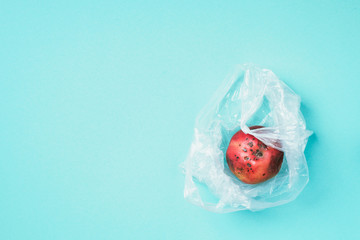Spoiled bad red apple in plastic bag on blue background. Garbage dump rotten food. Top view. Copy...