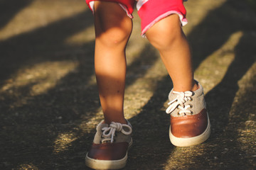 Kid legs wear on vintage shoes walking on the asphalt road, low angle