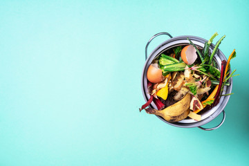 Sustainable and zero waste living. Vegetable waste in recycling compost pot. top view. Copy space. Peeled vegetables on chopping board, white compost bin on blue background. Recycle kitchen waste.
