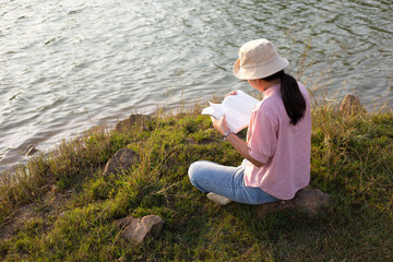 Fototapeta premium A young woman reading a book on the waterfront in the evening
