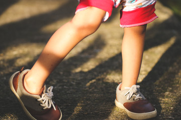 Kid legs wear on vintage shoes walking on the asphalt road, low angle