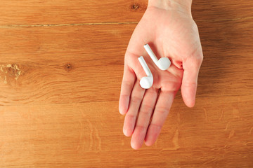 Female hands holding  wireless earphones on wooden background  top view  - Image