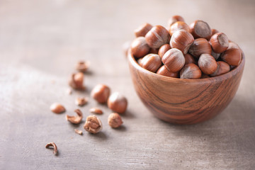 Obraz premium Hazelnuts in wooden bowl on wood textured background. Copy space. Superfood, vegan, vegetarian food concept. Macro of hazelnut, selective focus. Healthy snack.