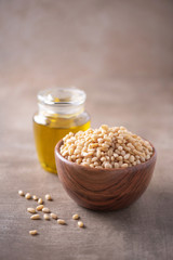 Shelled raw pine nuts in wooden bowl and pine nuts oil in bottle on wood textured background. Copy space. Superfood, vegan, vegetarian food concept. Macro of pine nuts texture, selective focus