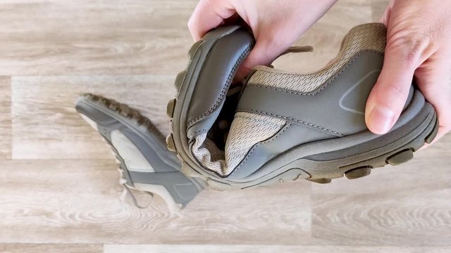 White hands squeeze gray sneaker. Test flexibility of rubber sole of sports shoes for fitness. Close-up, wooden background, faceless