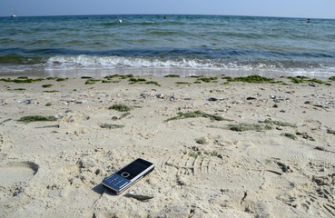 Fototapeta na wymiar mobile phone lying on the sand at the ocean beach