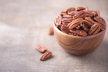 Pecan nuts in wooden bowl on wood textured background. Copy space. Superfood, vegan, vegetarian food concept. Macro of pecan nut, selective focus. Healthy snack
