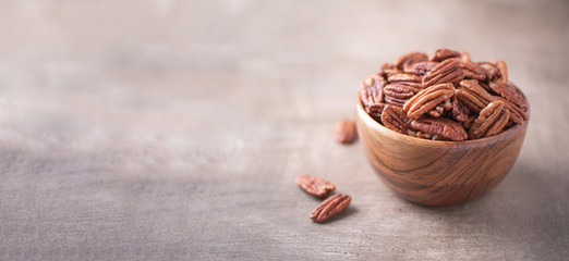 Pecan nuts in wooden bowl on wood textured background. Copy space. Superfood, vegan, vegetarian food concept. Macro of pecan nut, selective focus. Healthy snack
