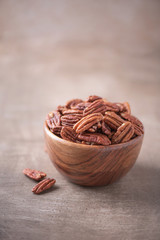 Pecan nuts in wooden bowl on wood textured background. Copy space. Superfood, vegan, vegetarian food concept. Macro of pecan nut, selective focus. Healthy snack