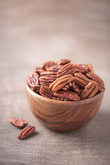 Pecan nuts in wooden bowl on wood textured background. Copy space. Superfood, vegan, vegetarian food concept. Macro of pecan nut, selective focus. Healthy snack