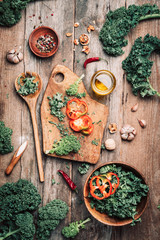 Fresh kale in bowl, wooden spoon, fork, chopping board, spices, salt, garlic, pepper on rustic wooden background. Top view. Copy space. Zero waste, organic vegetables concept. Vegan and vegetarian