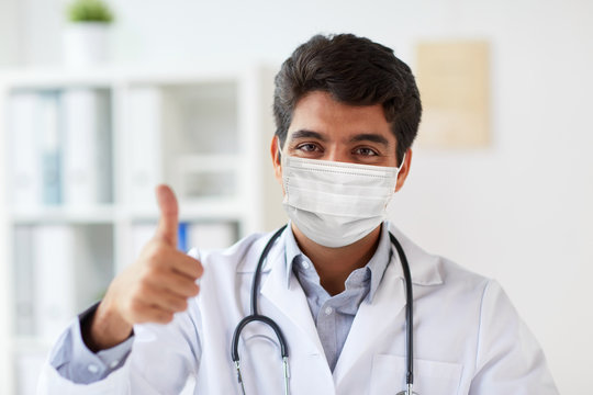 Medicine, Healthcare And Pandemic Concept - Indian Male Doctor With Stethoscope Wearing Protective Medical Mask For Protection From Virus Showing Thumbs Up At Clinic