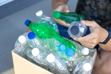 Hand  holding clear and green recyclable plastic bottle putting in paper garbage bin for recycling..waste management and plastic reuse to environmental protection world concept.