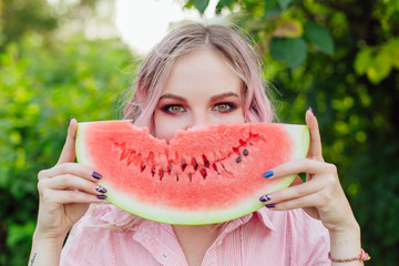 Beautiful young woman with pink hair holding juicy watermelon close to the face