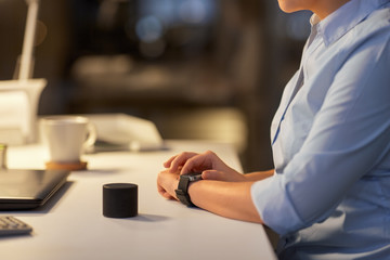 business, technology and internet of things concept - close up of businesswoman's hands with smart watch and speaker at night office