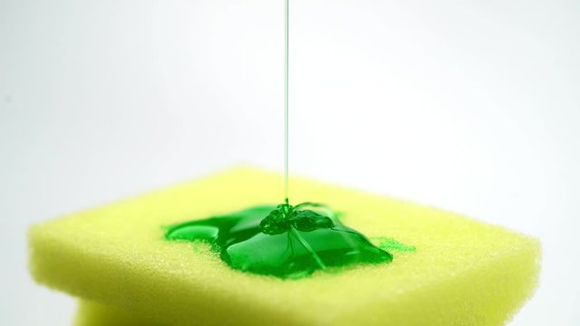 Super macro close up footage of yellow sponge for dish and pouring detergent in form of green gel.