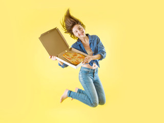 Beautiful young girl in jeans smiling holds a box of pizza on a yellow background