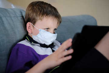 Schoolboy wearing a mask does schoolwork at home on a tablet device during the Covid-19 / coronavirus pandemic